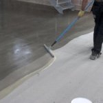 Professional applying a coat of grey epoxy over a prepared concrete surface.