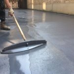 Contractor spreading tinted epoxy with a squeegee to create a smooth, even coat.